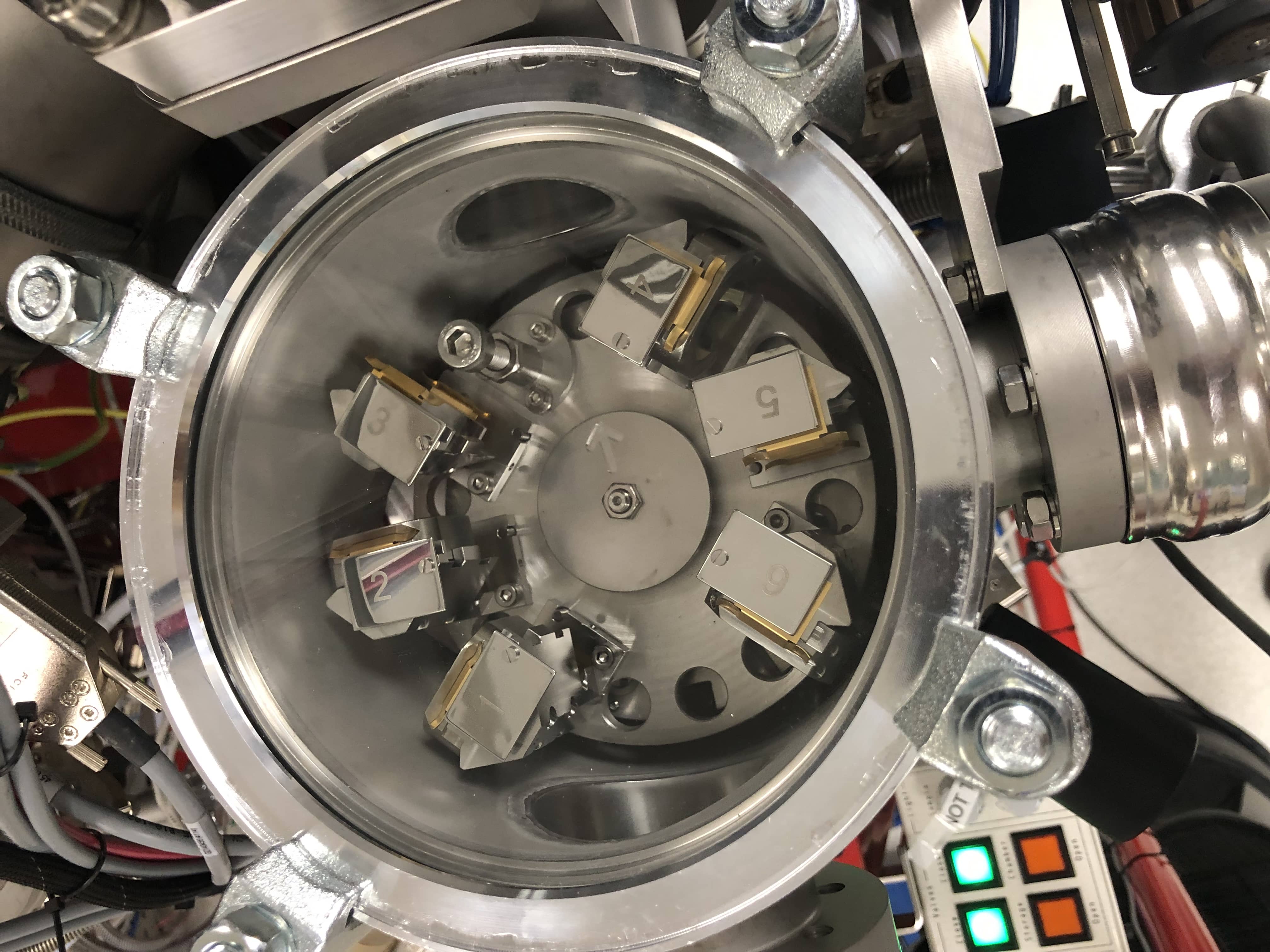 : The view from the top of a hollow metal cylinder looking down. At the bottom is a carousel holding six numbered metal cubes. On the sides are the openings to tunnels leading to different chambers of the instrument.