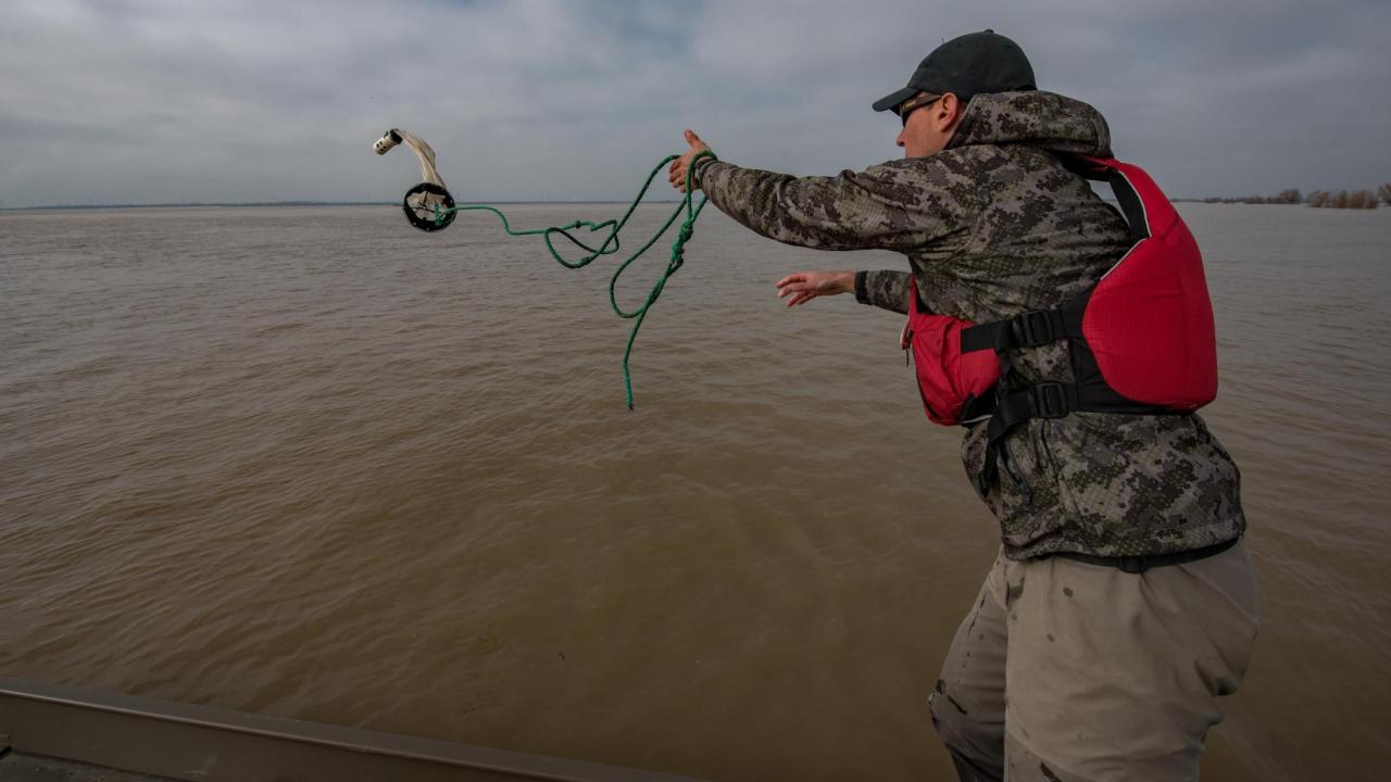 Person throws zooplankton net into floodplain. Net is mid-swing. 