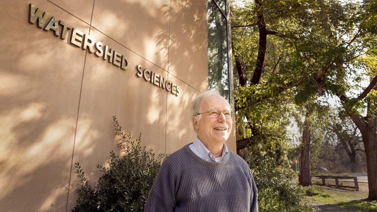 Jay Lund standing in front of the Center for Watershed Sciences building. He is under shaded trees and “Watershed Sciences” is written in gold on the building over his shoulder. Jay Lund and his wife, Jean Lund, have created an endowment at the Center for Watershed Sciences to encourage interdisciplinary water management research in student dissertations. (PC Karin Higgins/UC Davis). 