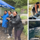 Three Winnemem Wintu fishery staff pose by the Nur Nature-Based incubation system. The setting is a damp wet forest beside a creek, mist is low. All three gesture towards the boxes while in the rain but the boxes under a rain cover.